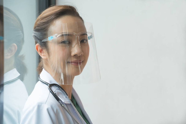 Asyalı kadın doktorlar, Gene 'in hastanedeki pencerenin yanında olduğu virüslerden korunmak için yüz koruyucu takıyorlar. Hastane personeli kavramı. - Fotoğraf, Görsel