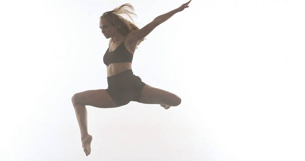 young beautiful female sporty dancer in black tights performing modern style ballet making acrobatic elements   female ballet dancer in art performance in front of white background - Foto, Imagen