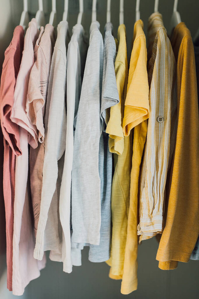 Variedade colorida de camisas, camisetas e blusas em cabides dentro de um guarda-roupa. Vestuário infantil para a coleção de verão. Moda infantil casual, roupas de algodão orgânico. Foco seletivo
. - Foto, Imagem