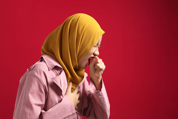 Asiatische muslimische Teenager-Mädchen bedecken ihren Mund beim Husten; vor rotem Hintergrund - Foto, Bild