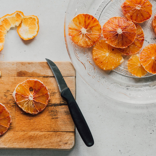 Delicious sliced blood oranges on rustic wooden cutting board, on white table. Healthy citrus snack to boost immunity. Colorful lifestyle top view, super foods concept. Flat lay with copy space. - Photo, Image