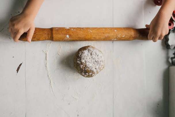 Raw dough on white kitchen table ready to be flattened with rolling pin on a Caucasian kid hands. Process of making a fruit tart or a french galette des rois crust. Top view, from above. Copy space. - Φωτογραφία, εικόνα