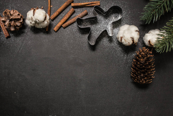 クリスマスの休日の精神の概念:ジンジャーブレッドの男や季節のビスケットフォーム、綿の花、松の小枝、コーン、シナモンスティックと黒の新鮮な雪の粉。創造的なフラットレイアウト。トップビュー、コピースペース. - 写真・画像