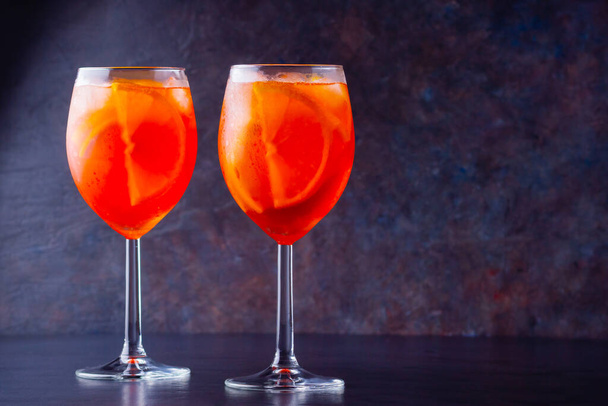 Aperol spritz cocktail in glass on dark background. Two glasses of aperol spritz with sliced orange. Summer cocktail in glass. Copy space - 写真・画像