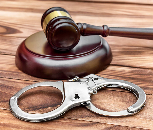 Handcuffs and judge's gavel with stand on wooden table. - Photo, Image