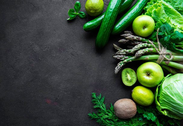 Здоровая вегетарианская еда концепция фона, свежая зеленая еда выбор для детоксикации диеты, яблоко, огурец, спаржа, авокадо, лайм, салат вид сверху на черном бетонном фоне - Фото, изображение