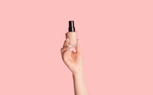 Gewassen weergave van millennial meisje tonen fles van make-up foundation op roze achtergrond - Foto, afbeelding