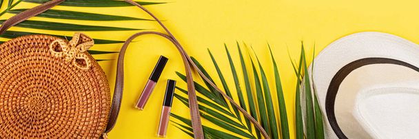 Summer composition. tropical palm leaves, straw bag, lipglosses on yellow background. Flat lay, top view, overhead, mockup, template, copy space - Fotoğraf, Görsel