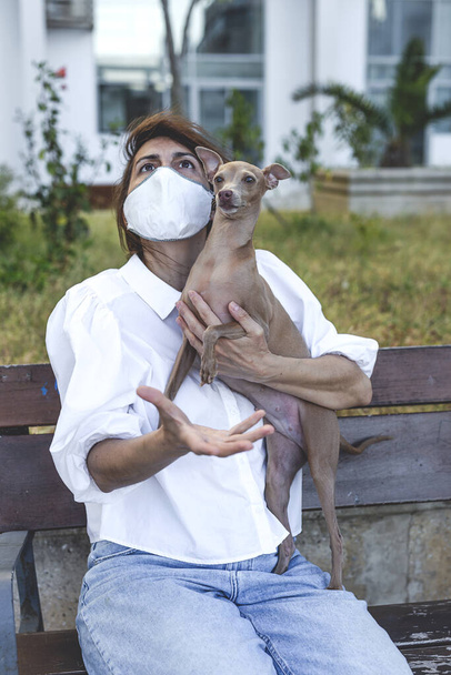 Woman playing with italian greyhound dog, with protective mask against coronavirus. Covid-19 concept - Foto, Imagen