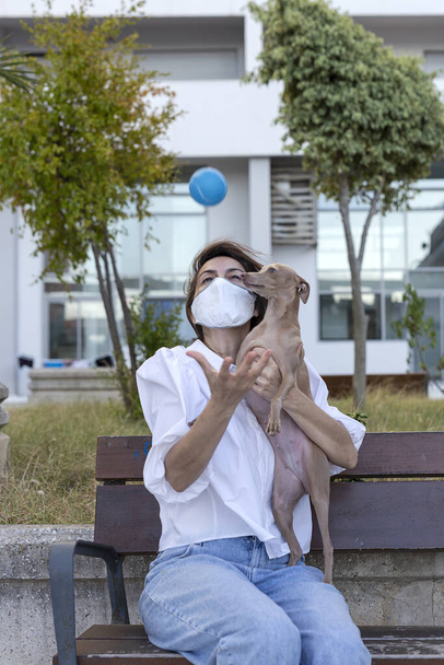 Woman playing with italian greyhound dog, with protective mask against coronavirus. Covid-19 concept - Фото, изображение