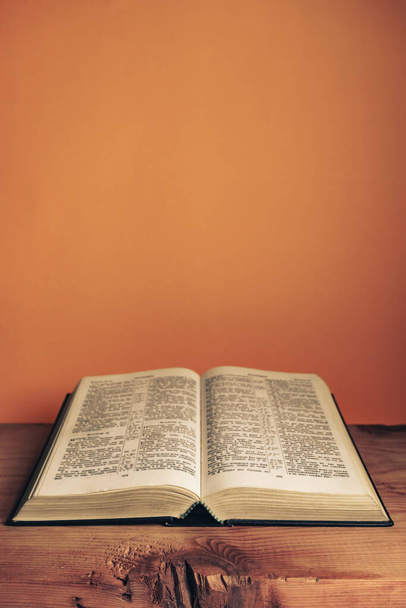 Open Holy Bible on a old wooden table. Beautiful orange wall background.	 - Φωτογραφία, εικόνα