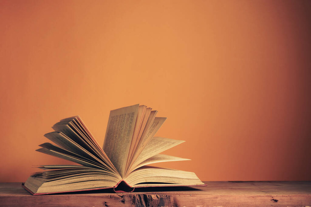 Bellissimo antico libro aperto su un tavolo di legno rosso e sfondo della parete arancione dietro. - Foto, immagini