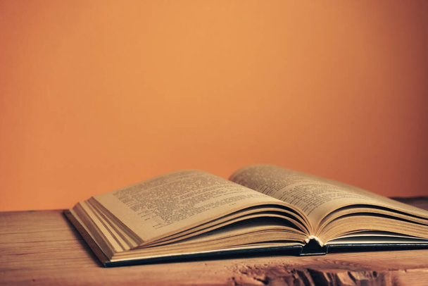 Nahaufnahme Schönes altes, offenes Buch auf rotem Holztisch und orangefarbenem Wandhintergrund. - Foto, Bild