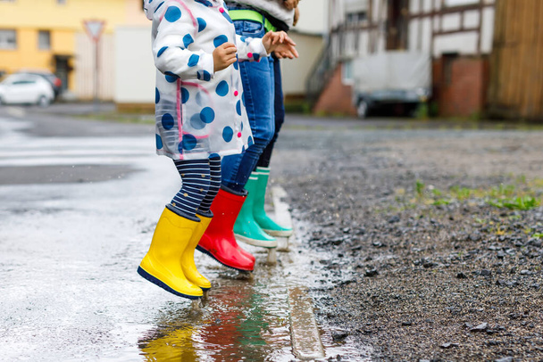 Primo piano di tre bambini, bambina e due ragazzi con gli stivali da pioggia rossi, gialli e verdi e che camminano durante la slitta. Fratelli felici che saltano nella pozzanghera. Divertimento all'aperto, famiglia attiva
 - Foto, immagini
