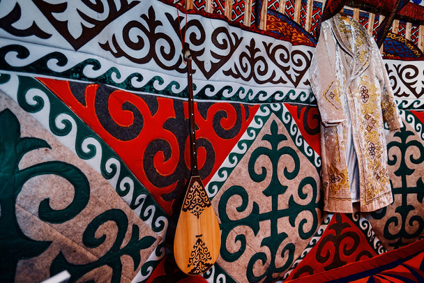 Traditioneel nationaal patroon in het Kazachse nationale huis, yurt. Op het tapijt is een Kazachse nationale strijkinstrument, dombra en een feestelijke kamerjas. - Foto, afbeelding