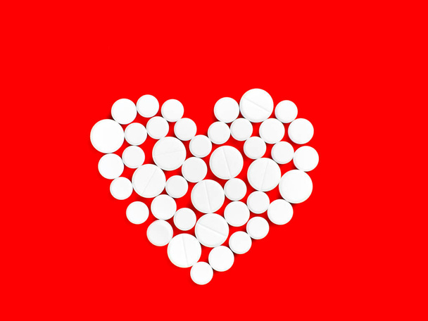 Witte medicijn pillen in de vorm van een hart op een rode achtergrond bovenaanzicht met kopieerruimte. - Foto, afbeelding
