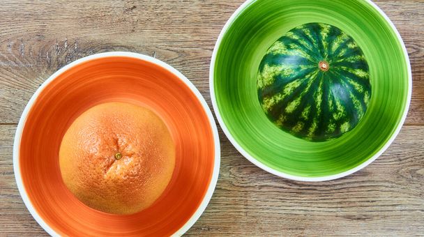 kleur stilleven - gele grapefruit op een oranje plaat en kleine watermeloen op een groene plaat op een houten tafelblad - Foto, afbeelding