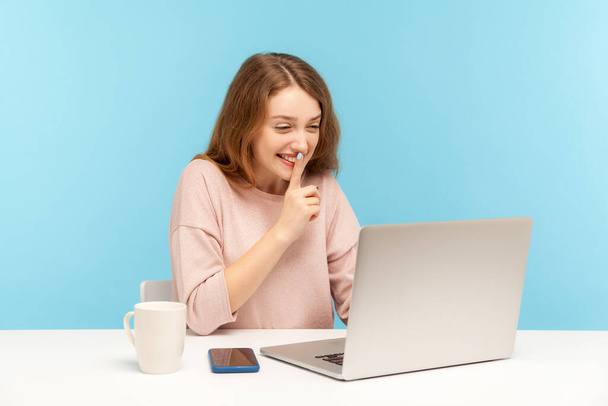 Please, keep secret. Positive young woman in casual clothes shushing with silence gesture, talking on video call, having online communication via laptop at home office. indoor studio shot isolated - Photo, Image