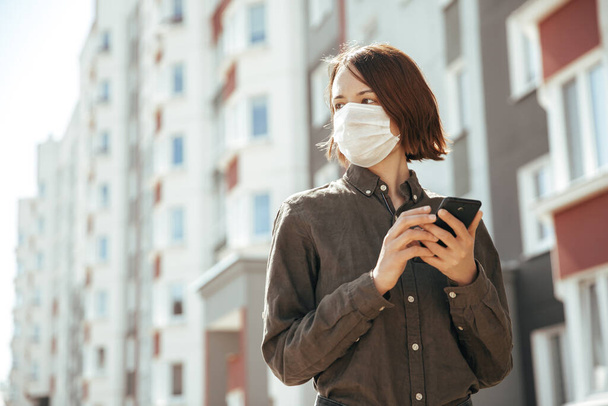 Girl holds a mobile phone and looks away. Masked girl smiling. - Foto, immagini