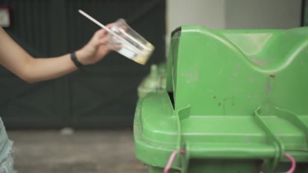Femmina mano smaltendo tazza di plastica trasparente sul cestino dei rifiuti verdi, luce naturale all'aperto, cestino, industria dei rifiuti di immondizia, spazzatura
  - Filmati, video