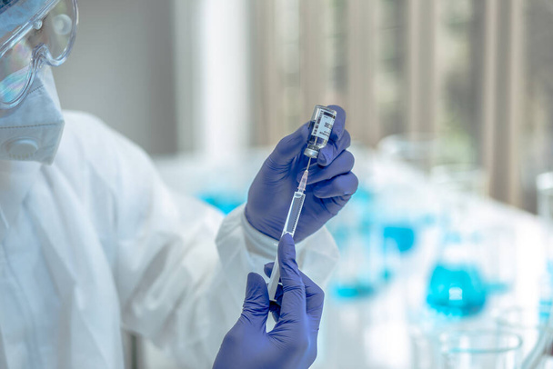 Científico o investigador mano en guantes azules que contienen gripe, sarampión, coronavirus, enfermedad de la vacuna covid-19 preparándose para los ensayos clínicos en humanos vacuna, medicina y concepto de medicamento. - Foto, imagen