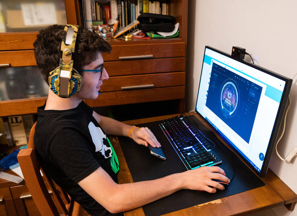 波状の茶色の髪とメガネを持つ白人の少年は、ゲームのヘッドフォンを身に着けている。ビデオゲームの動作に従うためにモニターの方への外観 - 写真・画像