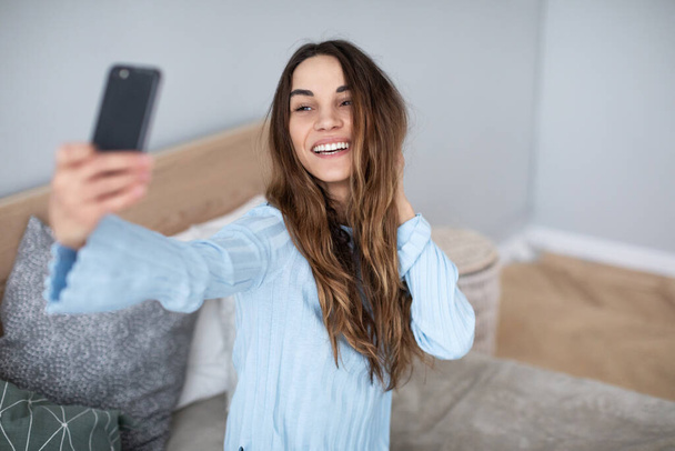 Cute young woman looking at her smartphone. Girl influencer posing for selfie. - Foto, immagini
