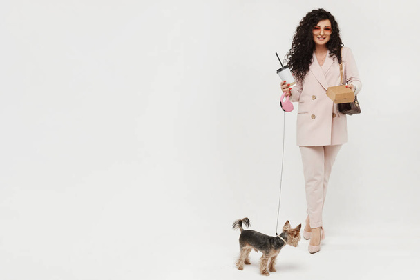 Modish woman with a plastic cup of coffee and cute little dog walking on white background, isolated. Urban fashion concept mockup. - Фото, изображение