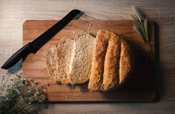 Home made and baked grain bread on a wooden table with black knife and floral decoration with copy space - Foto, afbeelding