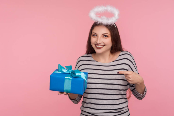 Portrait of happy angelic girl with saint halo over head pointing birthday gift and smiling, holding present, donating and offering surprise in box, congratulation on anniversary. studio shot isolated - Photo, Image