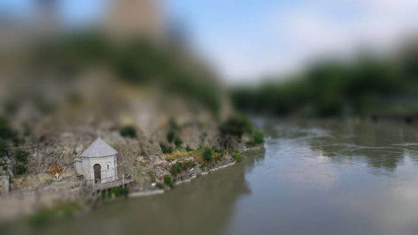 Tilt-Shift foto de la ciudad de Tiflis, Georgia. Antigua iglesia en el fondo de un acantilado en el río. Efecto miniatura
. - Foto, Imagen
