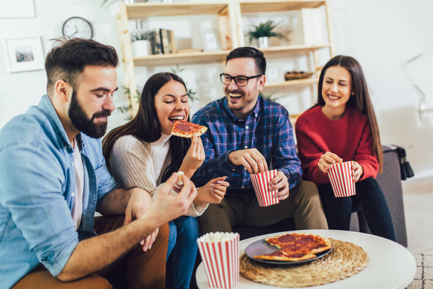 Grupo de jóvenes amigos comiendo pizza en el interior del hogar. Jóvenes divirtiéndose juntos
.  - Foto, imagen