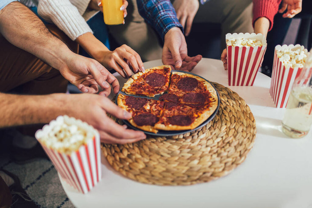 Hands of colleague or friends eating pizza and popcorn.  They are having party at home, eating pizza and having fun. - Photo, Image