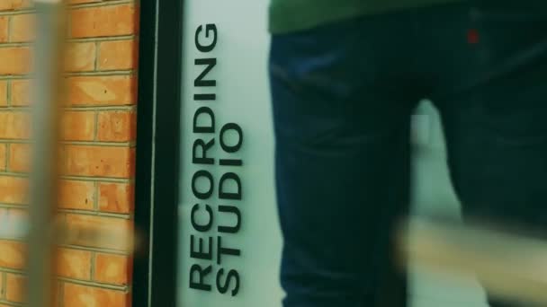 Um homem de jeans azul entra nos estúdios de gravação da porta
 - Filmagem, Vídeo