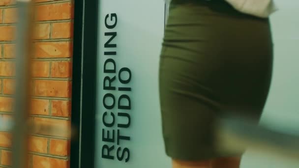 Kobieta w brązowej spódnicy wchodzi przez drzwi studia nagraniowego - Materiał filmowy, wideo