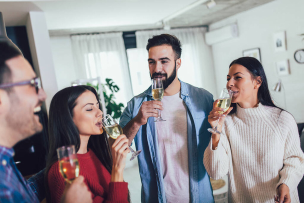 Jongeren juichen met champagne fluiten en op zoek gelukkig tijdens het hebben van home party. - Foto, afbeelding