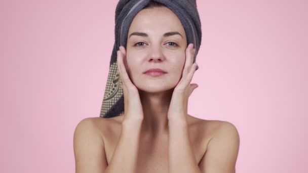 Woman with towel on her head looking at camera isolated on pink background - Video