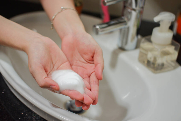 Femme asiatique à la peau claire montrant du savon en mousse pour les mains sur l'évier de la salle de bains. Fait preuve d'hygiène et de propreté pour prévenir la propagation du virus ou des bactéries
 - Photo, image