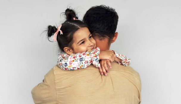 Rear View image of a handsome father hugging his daughter on the gray wall. Happy daughter and father feeling joyful. Dad and cute little girl embraces together, shares love on Father's Day. - Foto, Imagen