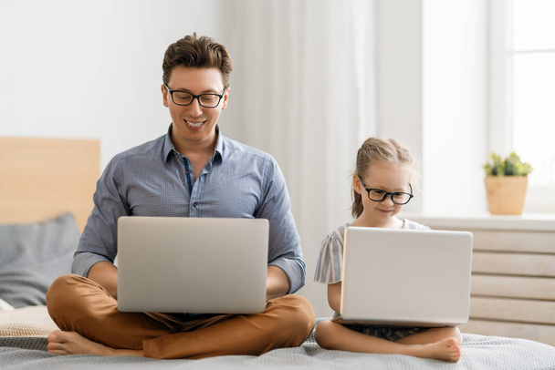 Happy loving family. Young father and daughter girl using laptops. Funny dad and lovely child are having fun staying at home. - Фото, изображение
