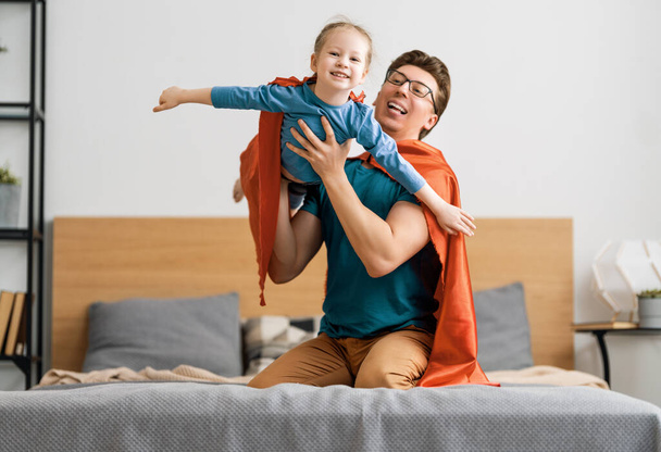 Father and his child playing together. Girl and dad in Superhero costume. Daddy and kid having fun, smiling and hugging. Family holiday and togetherness. - Foto, Imagen