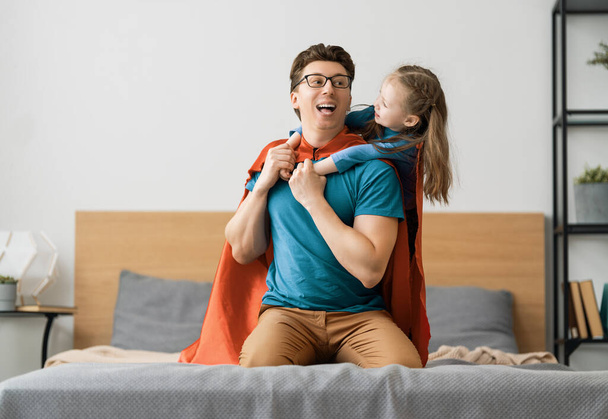 Father and his child playing together. Girl and dad in Superhero costume. Daddy and kid having fun, smiling and hugging. Family holiday and togetherness. - Фото, зображення