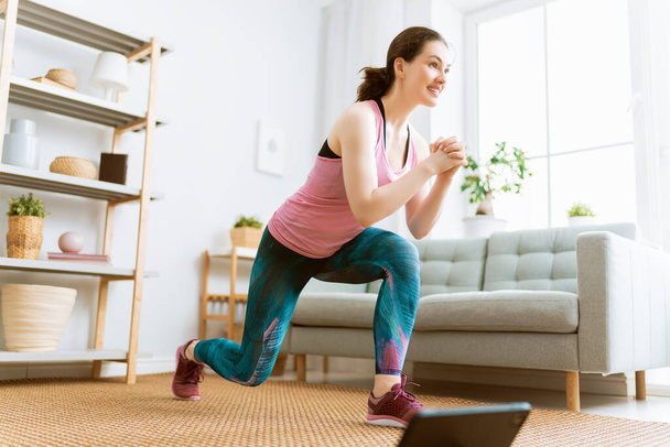Young woman in activewear watching online courses on tablet while exercising at home. - Foto, Imagem