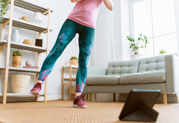 Young woman in activewear watching online courses on tablet while exercising at home. - Photo, image