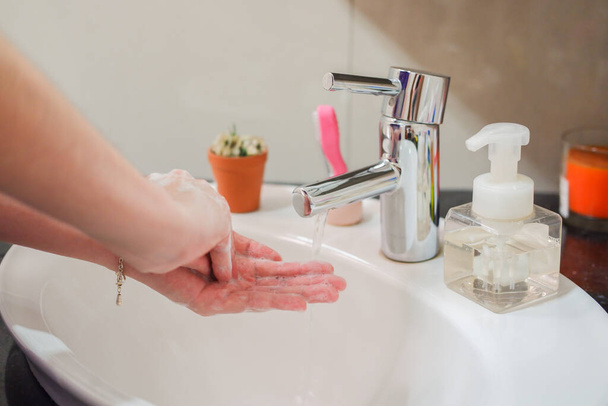 Μια ανοιχτόχρωμη Ασιάτισσα πλένει αφρώδη χέρια στο νιπτήρα του μπάνιου με σαπούνι. Δείχνει υγιεινή και καθαριότητα για την πρόληψη της εξάπλωσης του ιού ή των βακτηρίων - Φωτογραφία, εικόνα