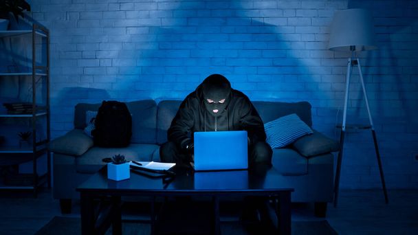 Masked hacker downloading private information using laptop - Photo, Image
