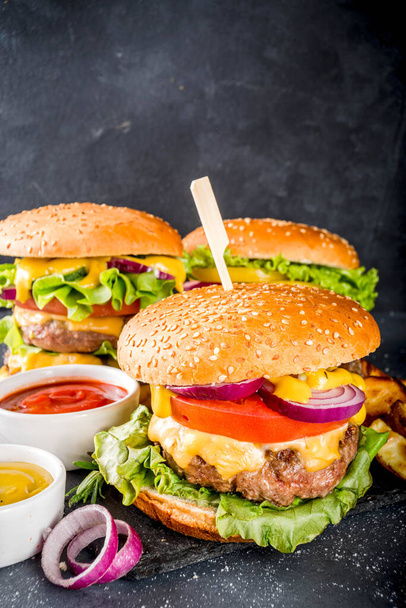 Tasty grilled homemade cheeseburgers with beef, tomato, cheese, tomato and lettuce. On dark grey background, with sauces. Top view copy space - Foto, Imagen