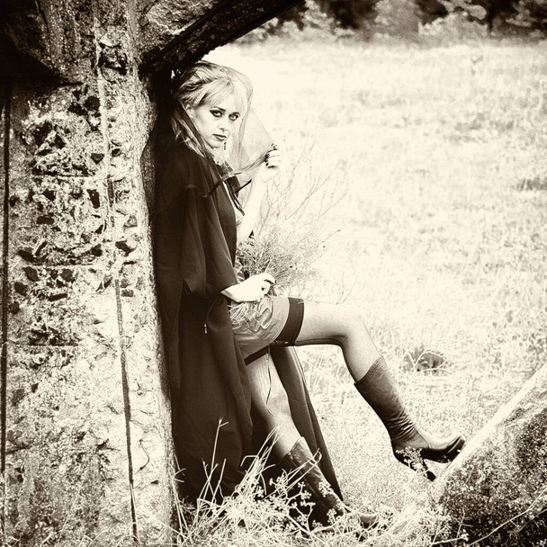 mystérieuse femme blonde sexy dans une robe rouge et manteau noir, avec un voile noir sur la tête. dans la nature à côté d'un vieux bâtiment presque détruit. Style gothique. Mode
. - Photo, image