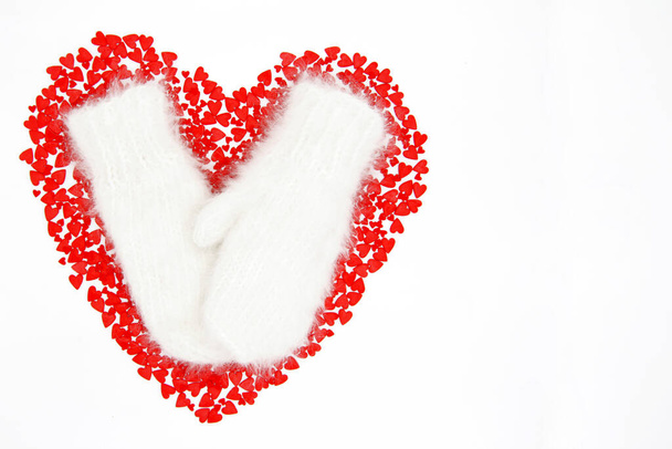 Many small scattered hearts in the shape of a large heart, on top of white warm woolen mittens. Red hearts for Valentine's Day. Christmas. The view from the top. Flatly. Copy space. - Foto, Imagem