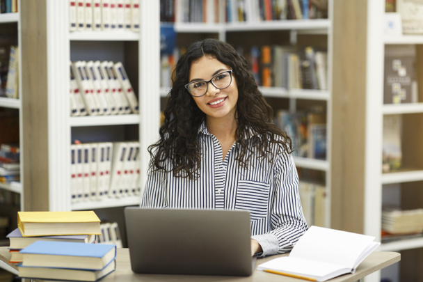 Usmívající se latina dívka pomocí notebooku v moderní knihovně - Fotografie, Obrázek